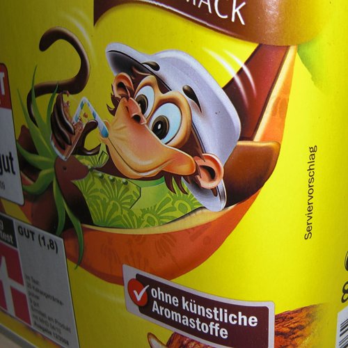 Foto der Packung eines Kakaogetränkepulvers, auf dem ein Affe mit Hut in einer Hängematte liegt und durch einen Strohhalm Kakao trinkt. Daneben der Schriftzug „Serviervorschlag“.